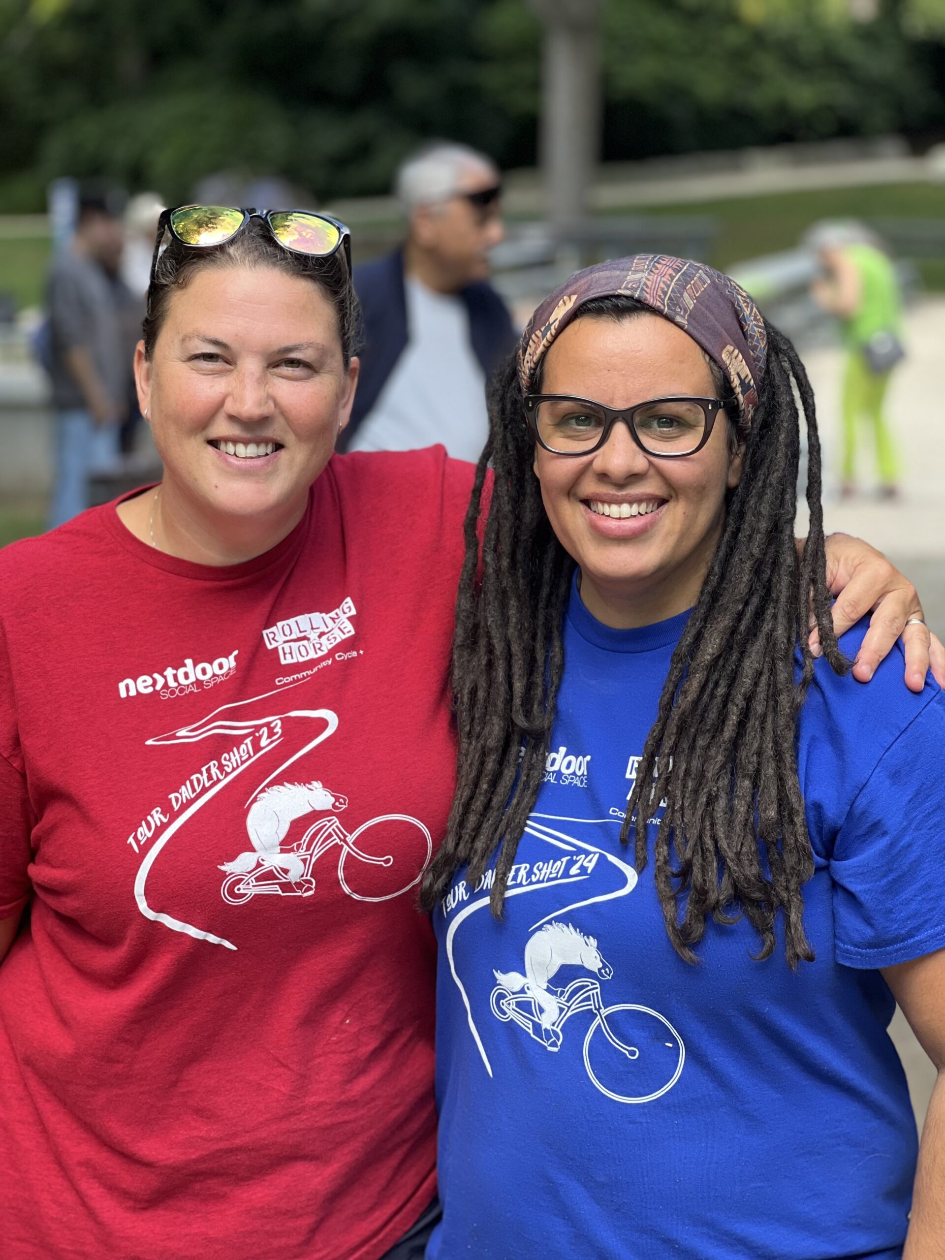 Two woman smiling with bike riders in the background